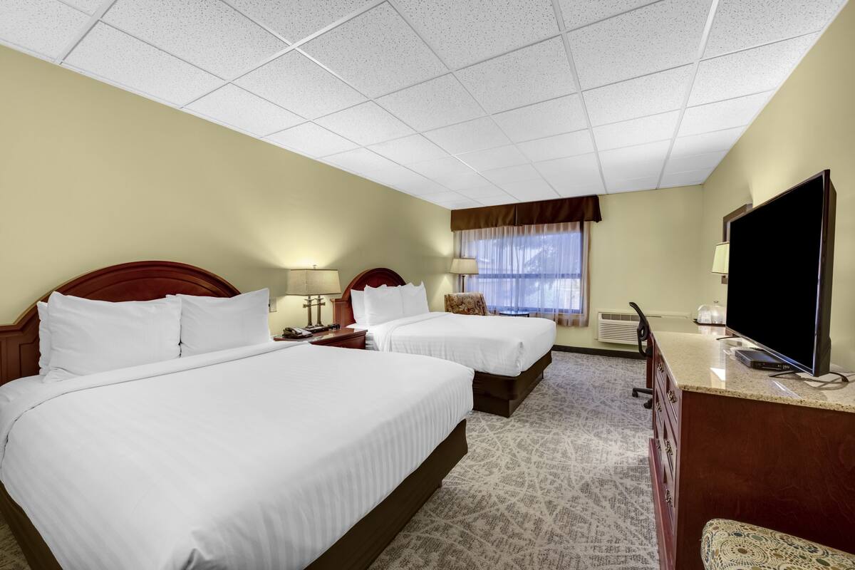 A hotel room with two beds, a TV, a desk, and a window with curtains.