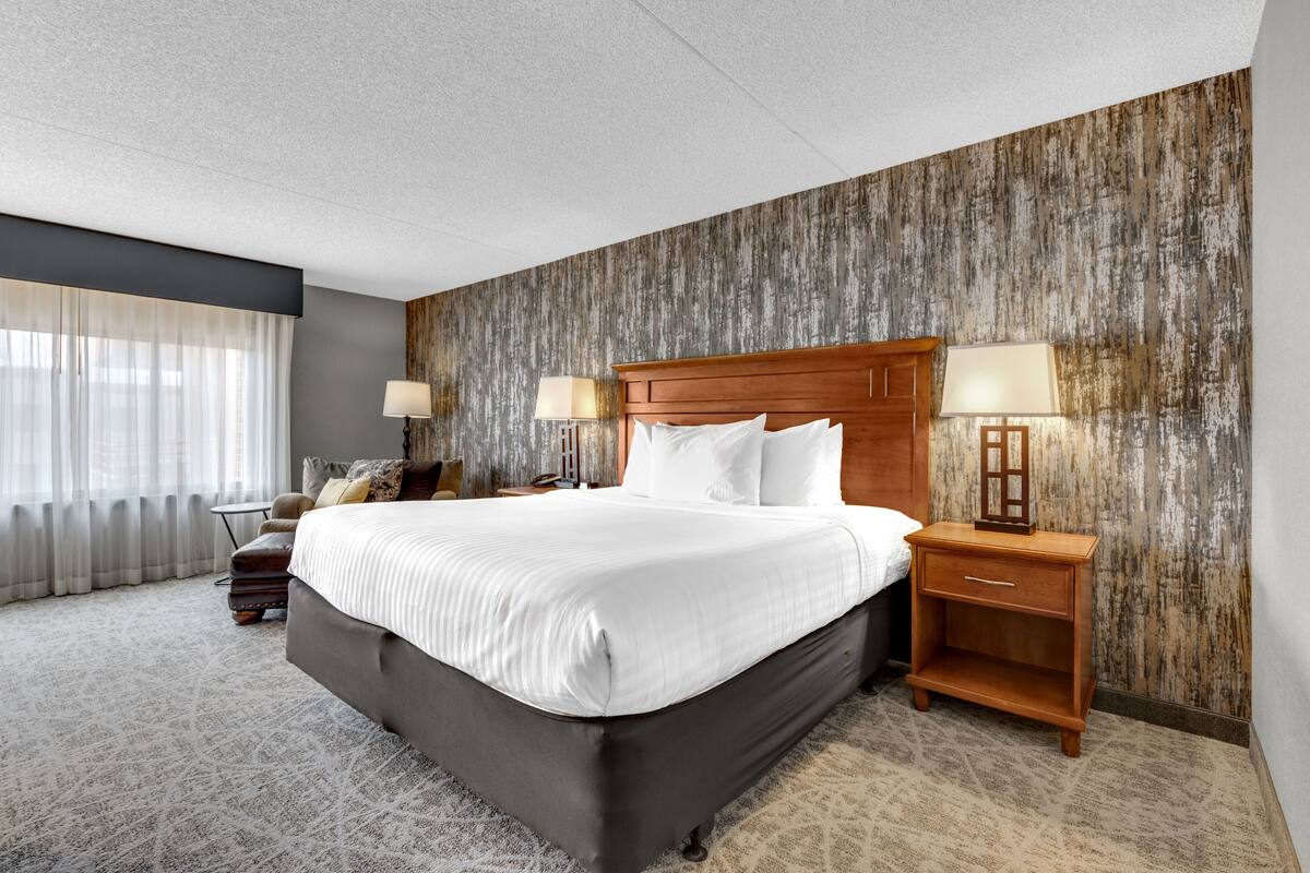A hotel room with a large bed, two bedside tables with lamps, a wooden headboard, and a textured wall.