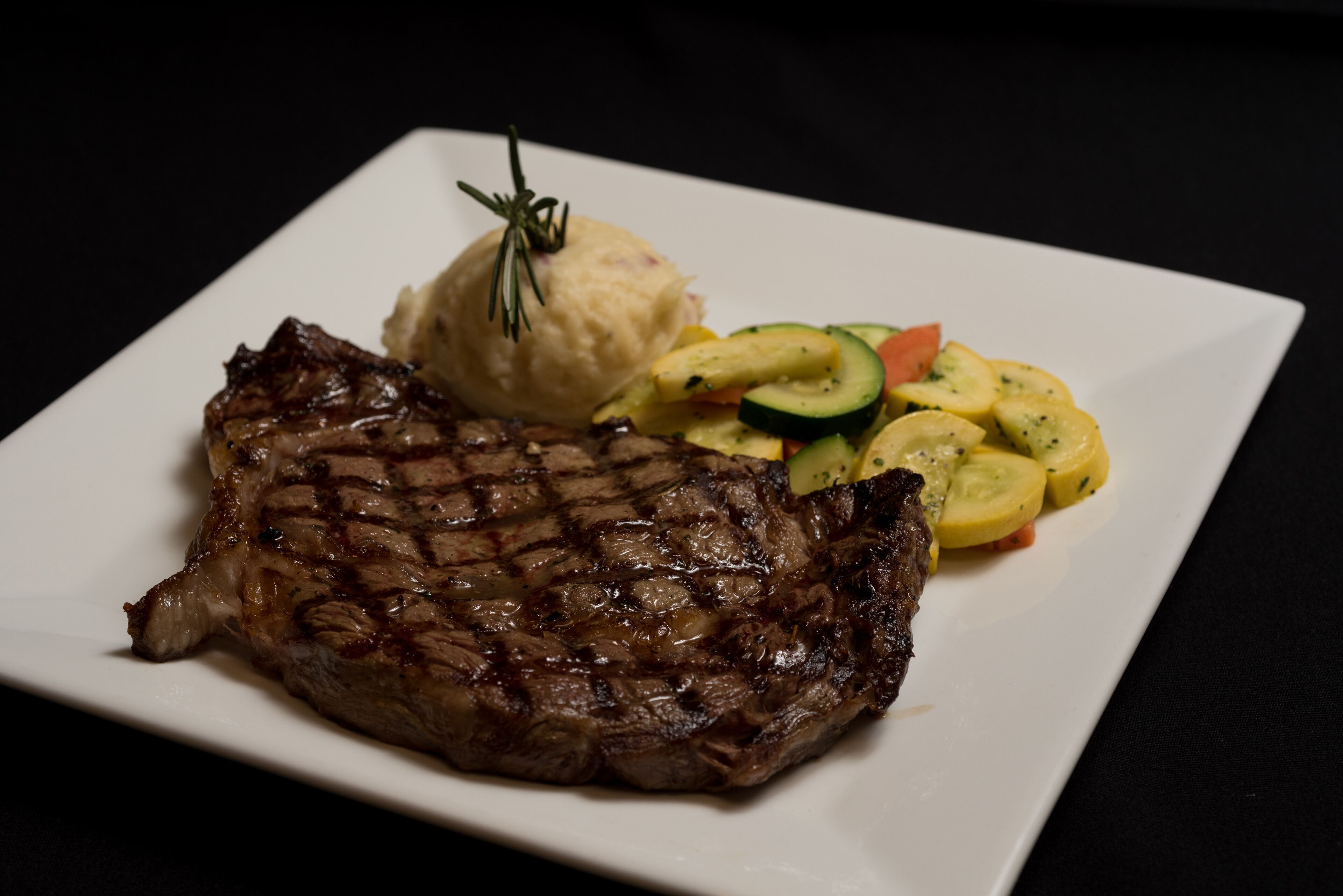 A plate with a grilled steak, mashed potatoes, and a side of sliced vegetables.