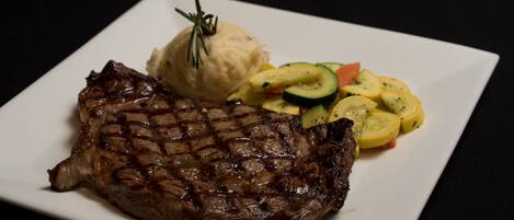 A plate with a grilled steak, mashed potatoes, and a side of sliced vegetables.