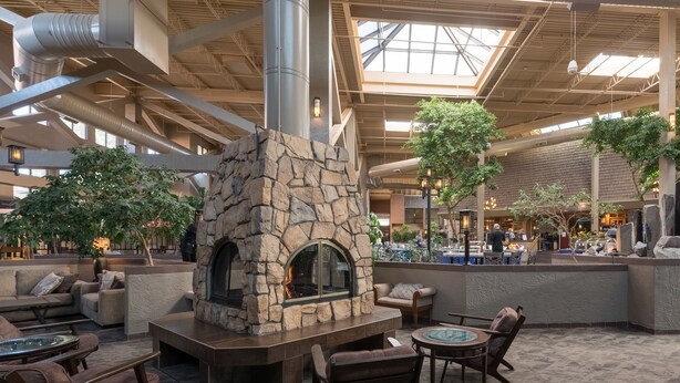 A spacious indoor area with a stone fireplace, comfortable seating, and a high ceiling with skylights. - The Academy Hotel Colorado Springs (Colorado Springs)