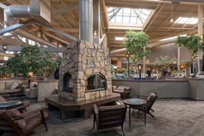 A spacious indoor area with a stone fireplace, comfortable seating, and a high ceiling with skylights. - The Academy Hotel Colorado Springs (Colorado Springs)