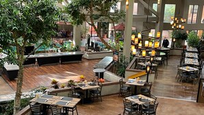 An indoor dining area with multiple tables and chairs, a central bar area, and potted plants. - The Academy Hotel Colorado Springs (Colorado Springs)
