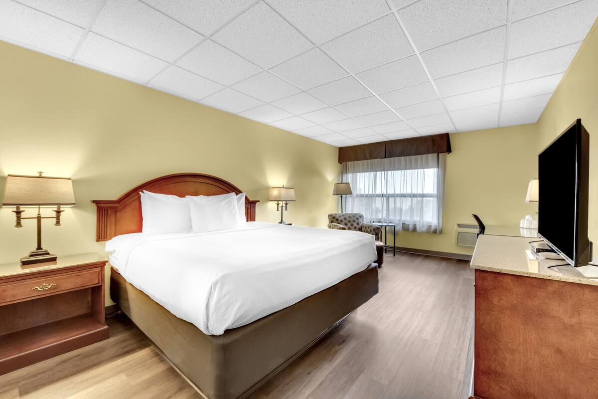 A hotel room with a large bed, bedside lamps, a desk with a flat-screen TV, and a window with curtains.