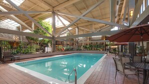 An indoor swimming pool with tiled flooring, metal railings, and outdoor seating areas. - The Academy Hotel Colorado Springs (Colorado Springs)