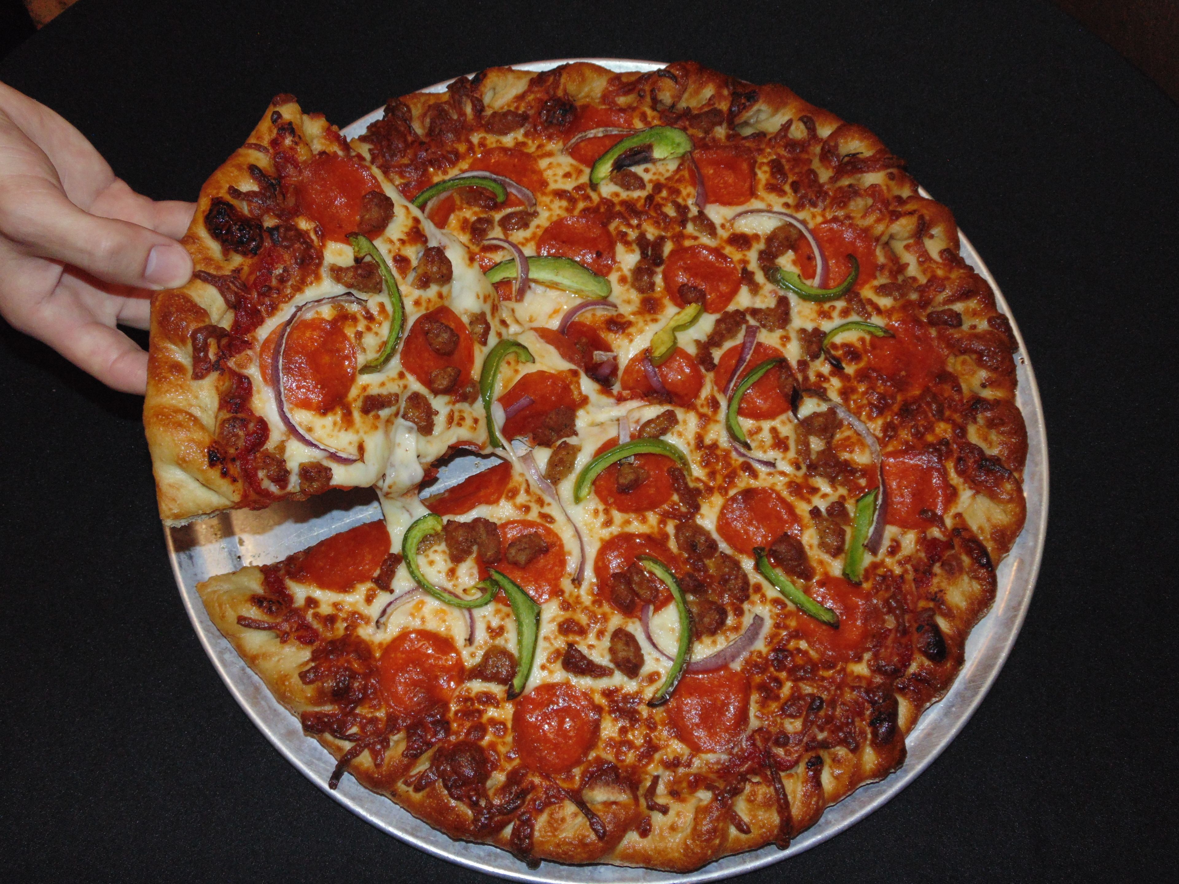 Una pizza con pepperoni, pimientos verdes y cebollas sobre una bandeja metálica.