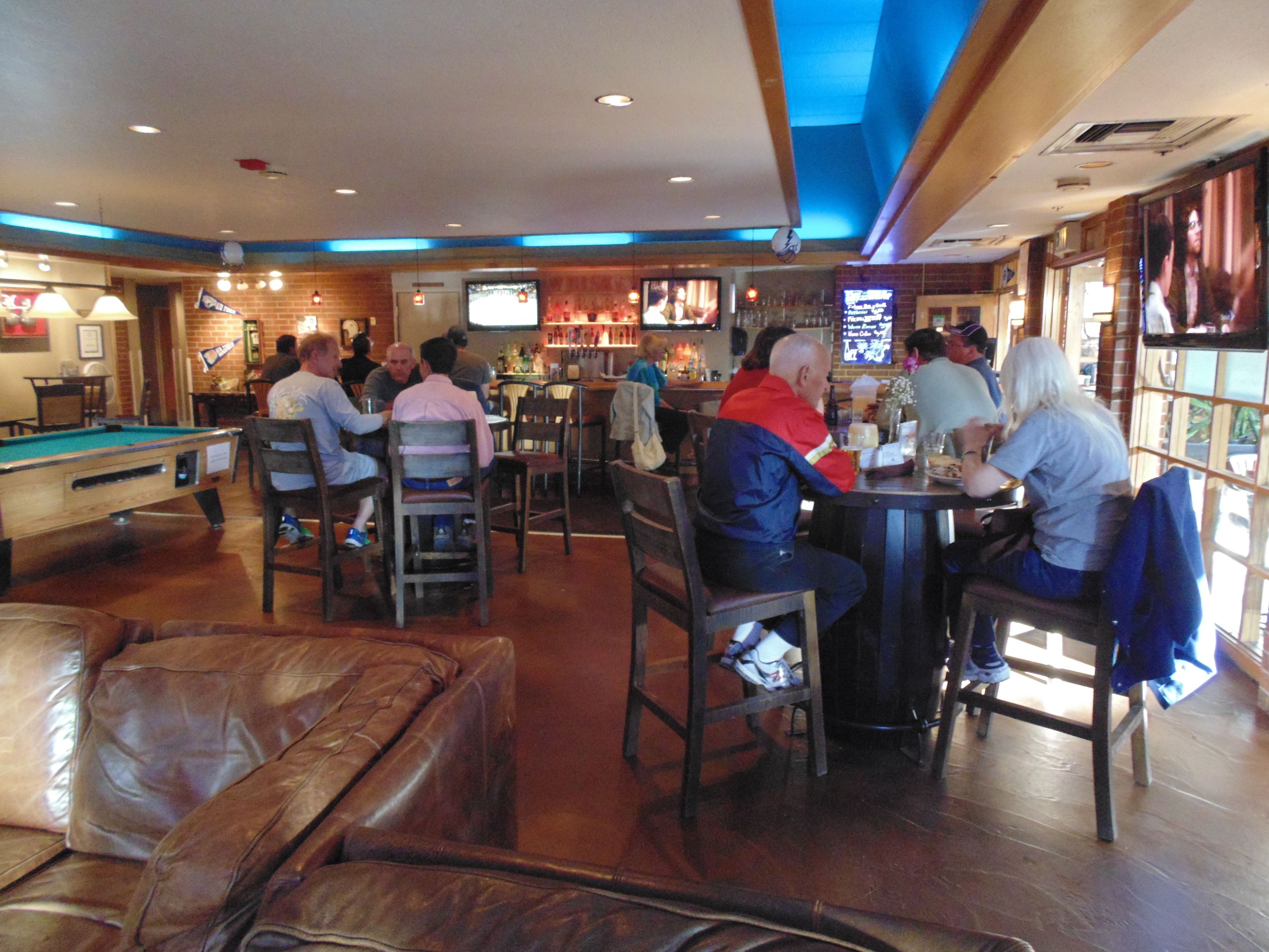 A bar with pool tables, seating, and a television screen.