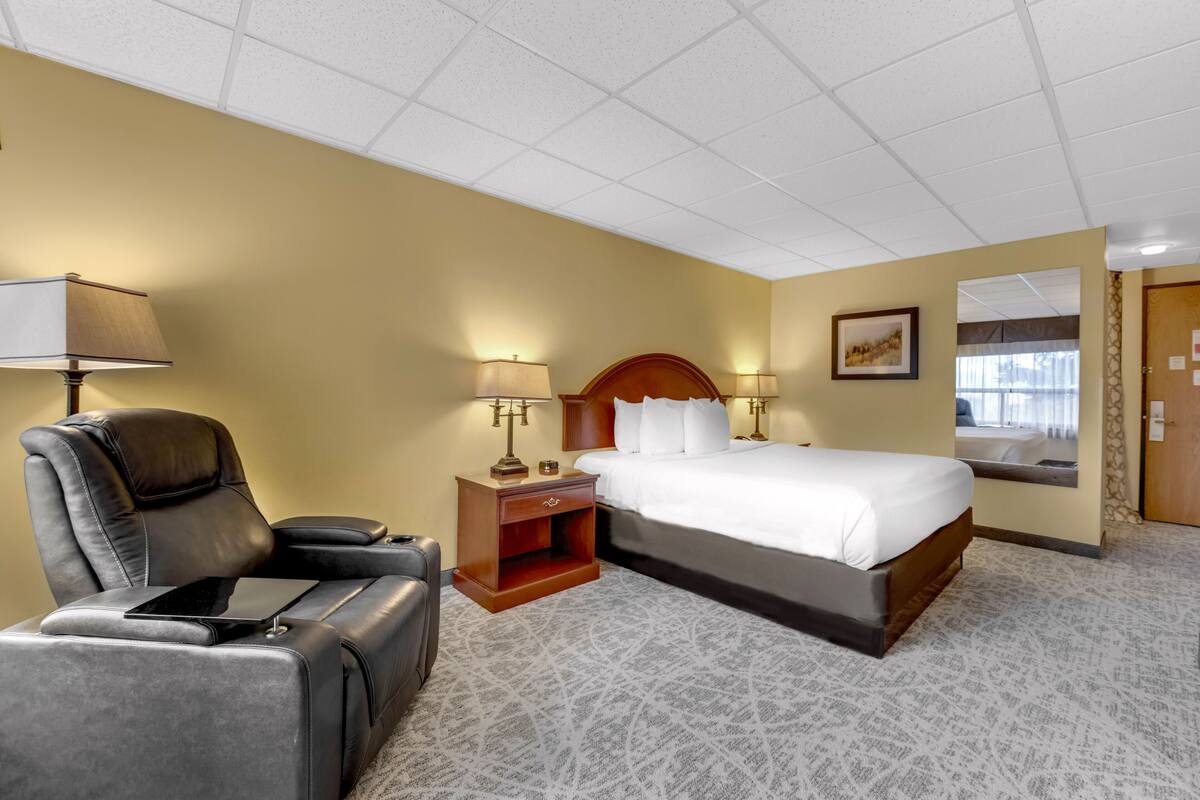 A hotel room with a bed, a chair, a nightstand, and a lamp.
