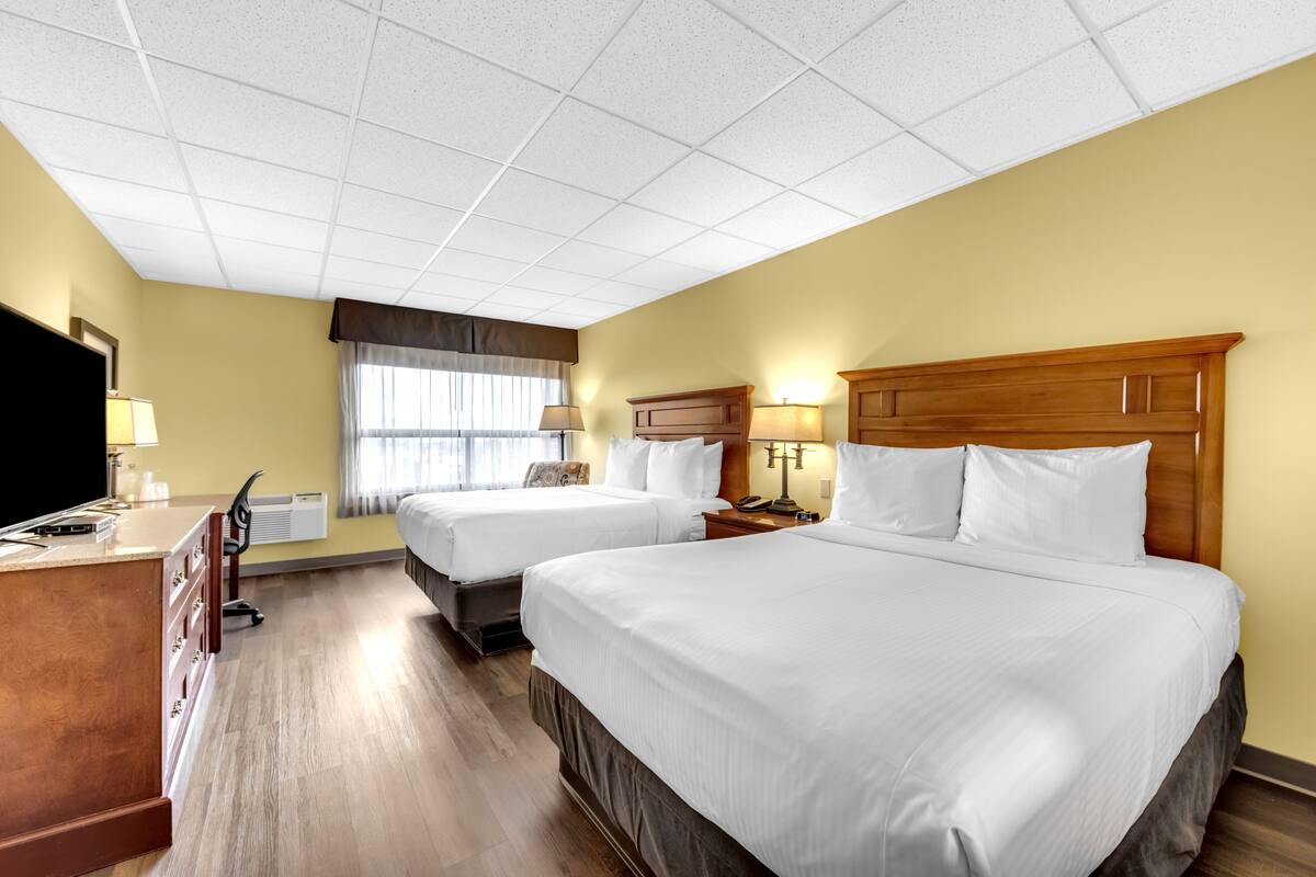 A hotel room with two beds, a desk, a TV, and a window with curtains.