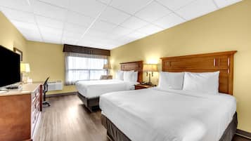A hotel room with two beds, a desk, a TV, and a window with curtains.