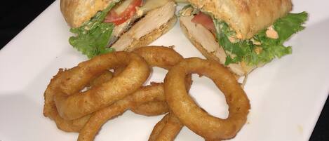 A sandwich cut in half with lettuce, tomato, and a creamy filling, accompanied by onion rings on a white plate.