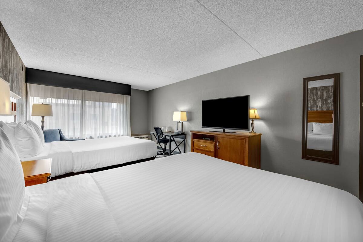 A hotel room with two beds, a desk, a chair, a television, and a mirror.