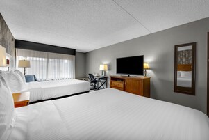 A hotel room with two beds, a desk, a chair, a television, and a mirror.