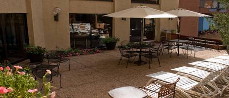 An outdoor patio with tables and chairs, surrounded by potted plants and flowers.