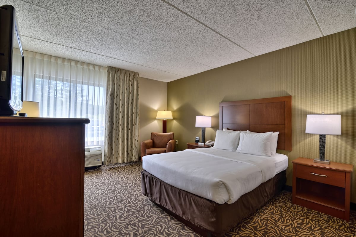 A hotel room with a large bed, two bedside tables with lamps, a wooden nightstand, a chair, and a desk with a lamp.