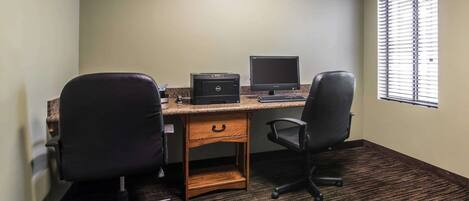 A small office with two black office chairs, a wooden desk, a desktop computer, and a window with blinds.