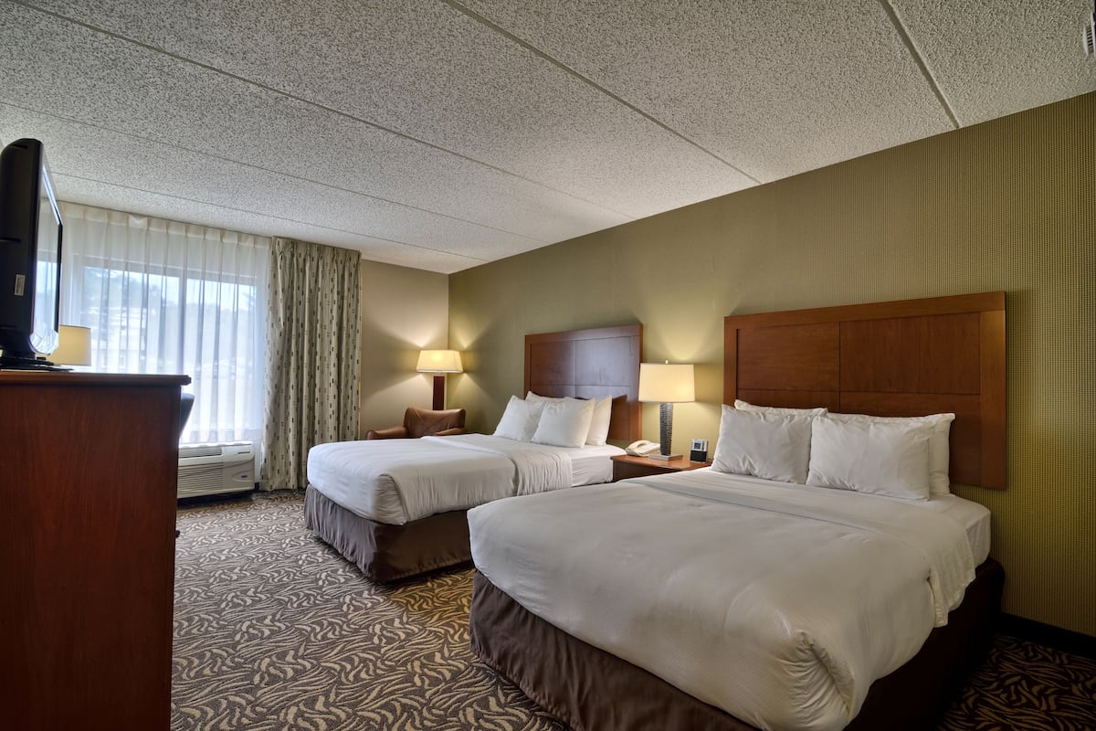 A hotel room with two beds, a desk, a telephone, and a window with curtains.