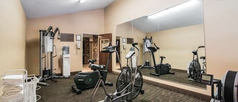 Un gimnasio de hotel con equipo de ejercicio, un espejo y piso alfombrado.