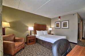 A hotel room with a bed, two bedside lamps, a brown leather armchair, a wooden nightstand, and a patterned carpet.