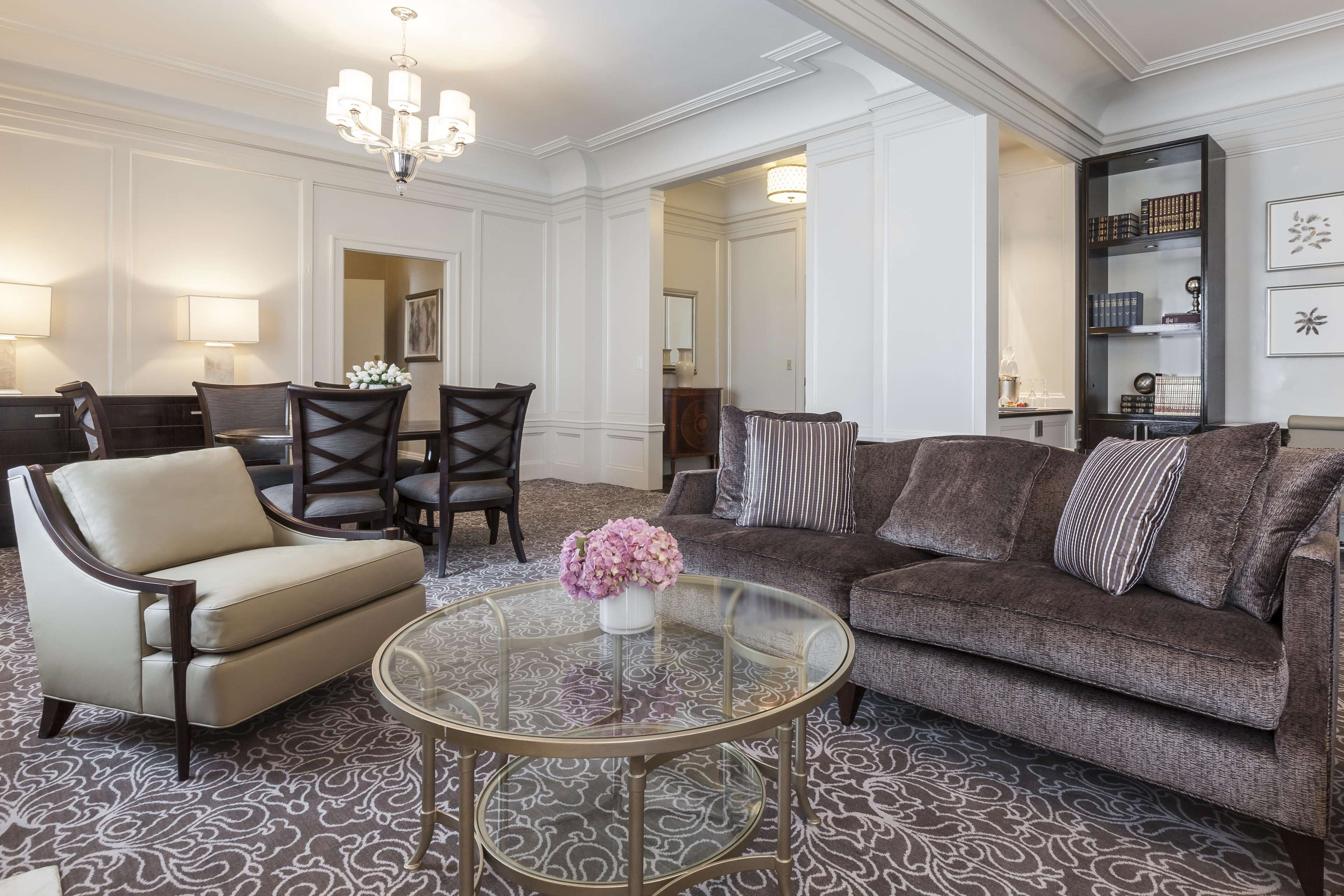 Un salon avec une table basse ronde en verre, un fauteuil beige, un canapé marron foncé et un lustre.