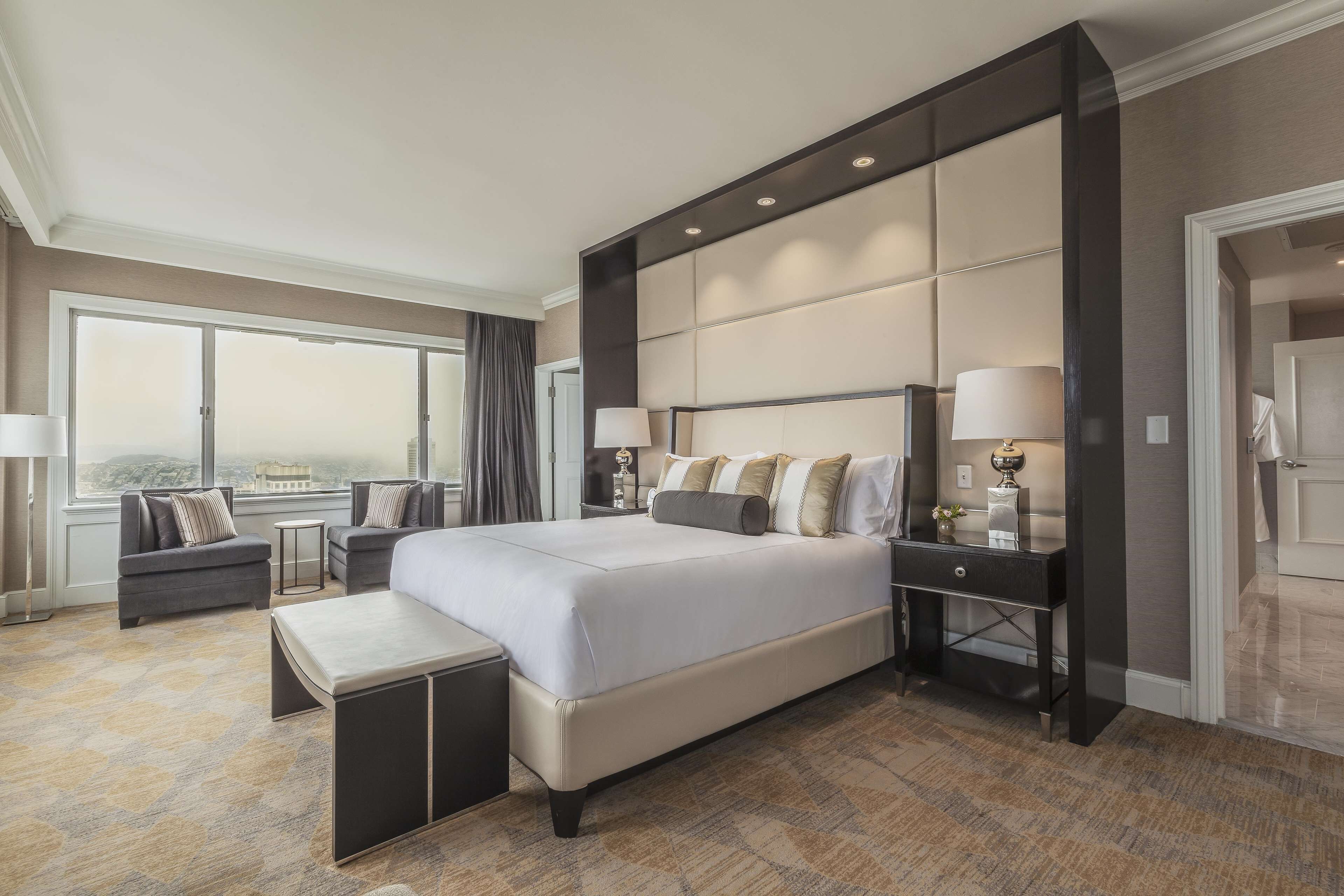 A spacious hotel room with a large bed, a sofa, a desk, and a view of the city.
