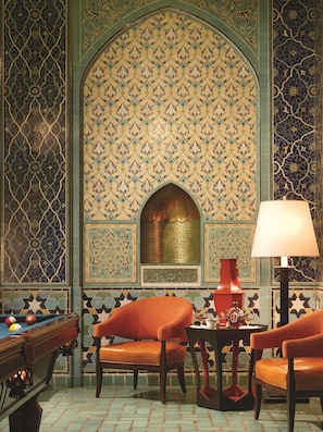 A room with a pool table, two orange chairs, a lamp, and a decorative wall with intricate patterns.