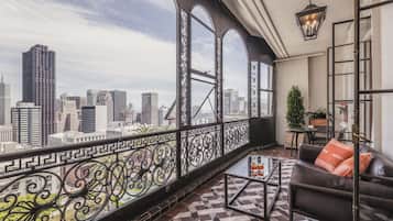 Un balcón con vista a la ciudad, un sofá de cuero, una mesa de centro de vidrio y una barandilla decorativa de hierro.