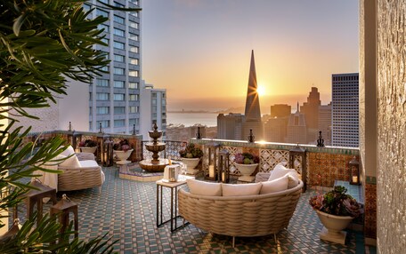 A rooftop terrace with a city skyline, a fountain, and outdoor seating.