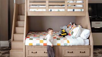 A bunk bed with a wooden ladder, a child standing beside it, and a television in the room.