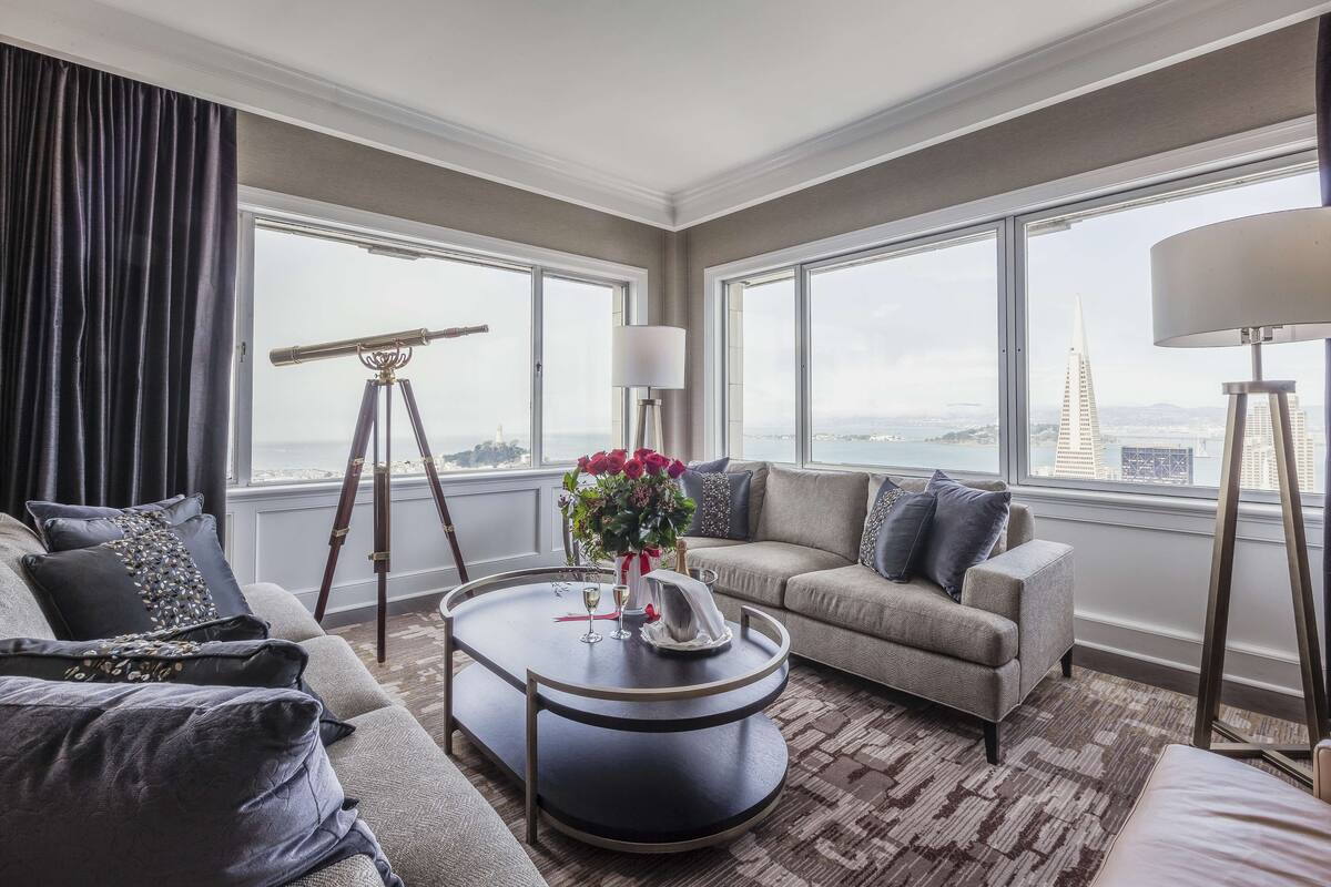 A modern hotel room with a large window, a round coffee table, a sofa, and a telescope.