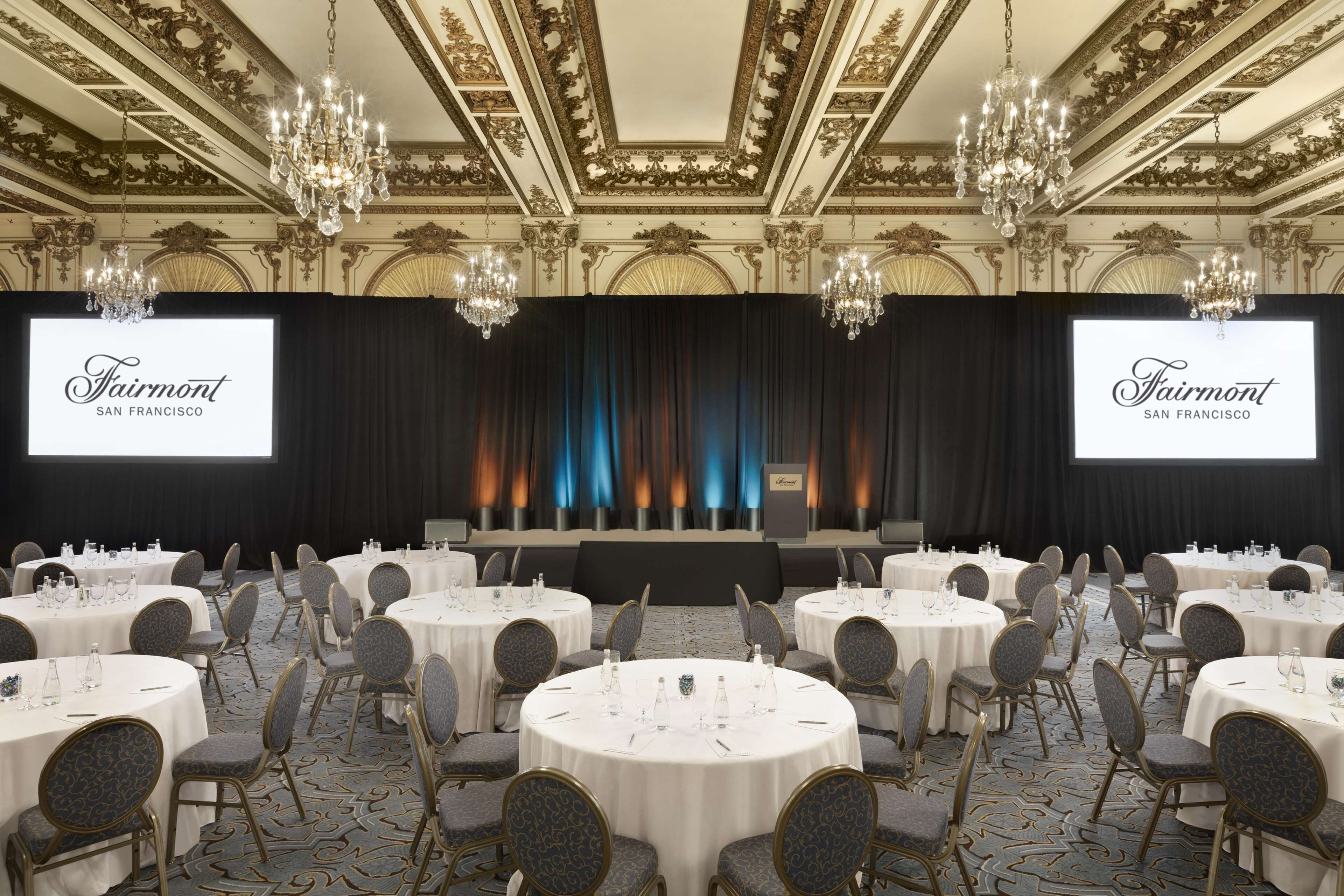 A conference room with round tables, chairs, and a stage with a backdrop.