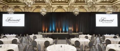A conference room with round tables, chairs, and a stage with a backdrop.