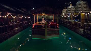 A boat-shaped bar with a thatched roof, surrounded by a water canal with string lights.