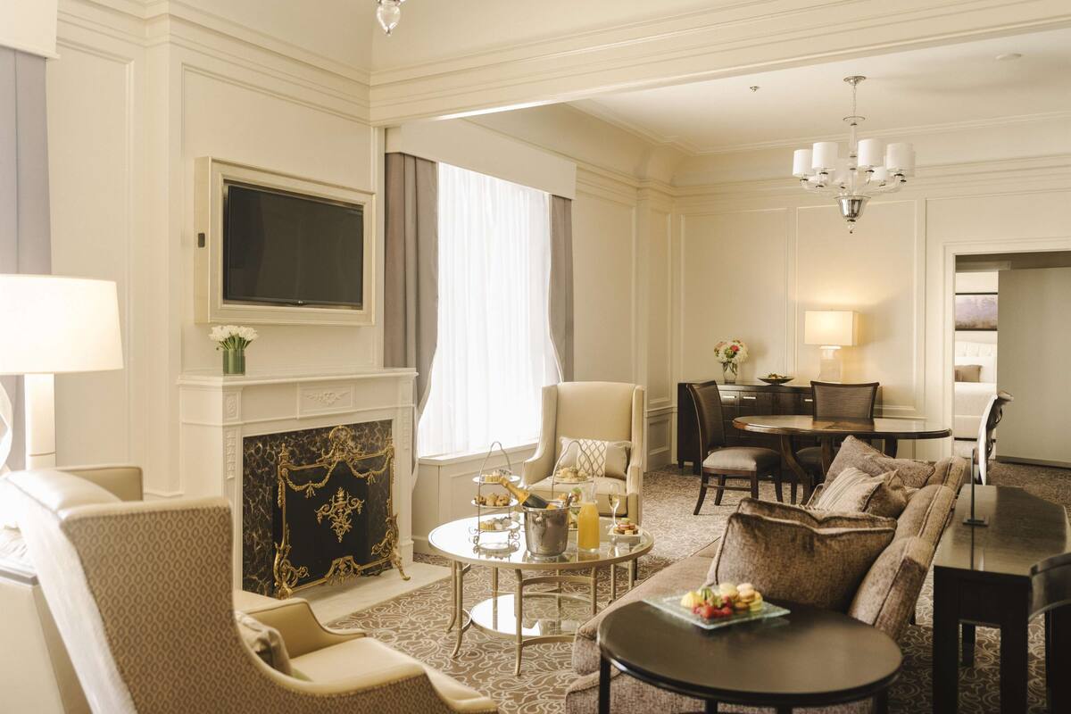A spacious living room with a fireplace, comfortable seating, a dining area, and a TV mounted on the wall.