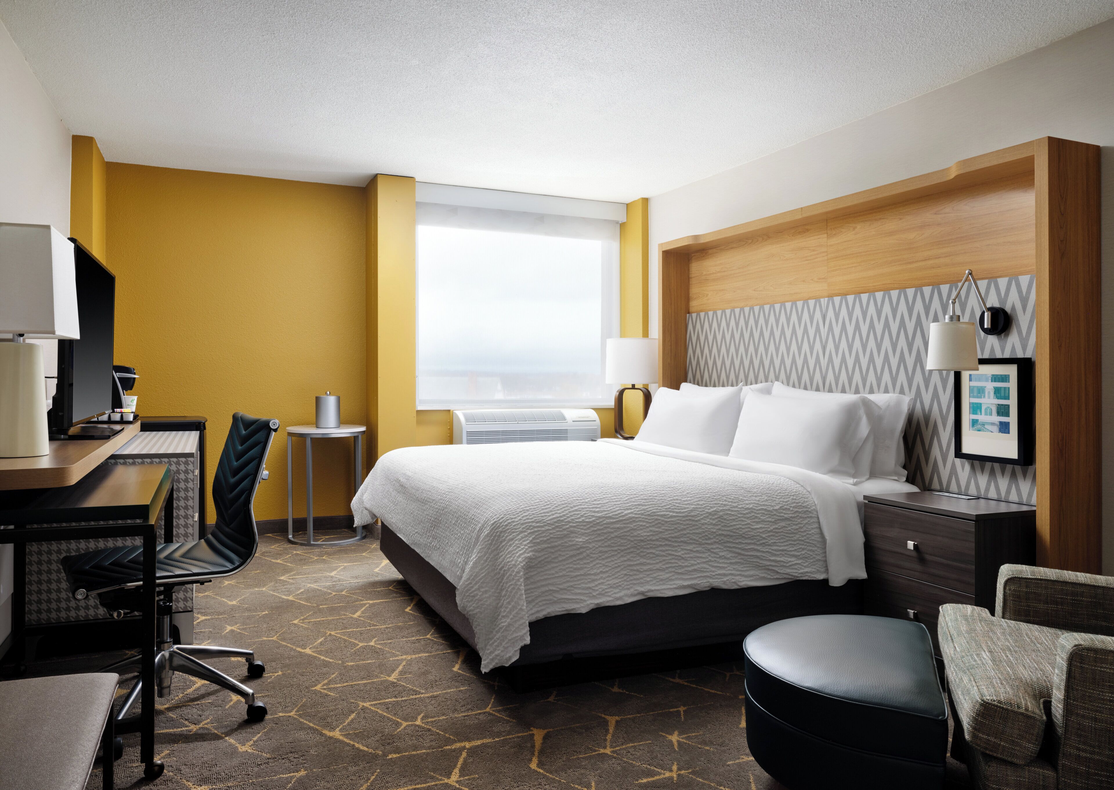Een hotelkamer met een bed, een bureau, een stoel, een klein tafeltje en een raam.