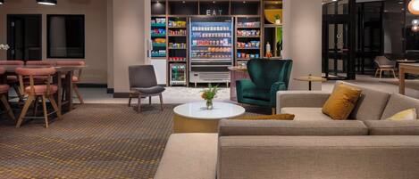A hotel lobby with a seating area, a refreshment kiosk, and a vending machine.