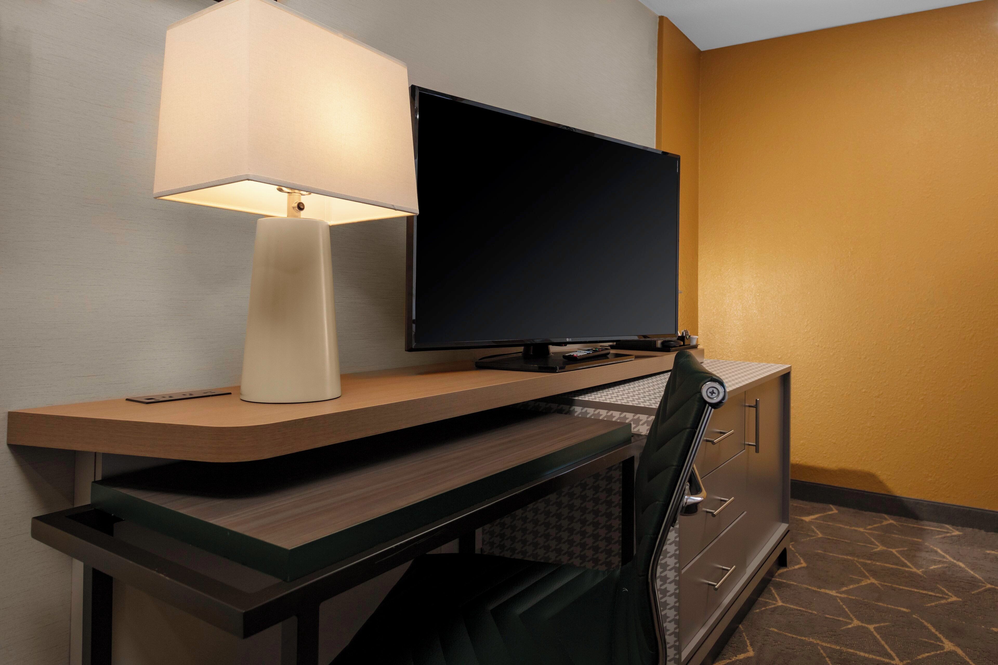 Une chambre d’hôtel équipée d’un bureau, d’une télévision à écran plat, d’une lampe et d’une chaise.