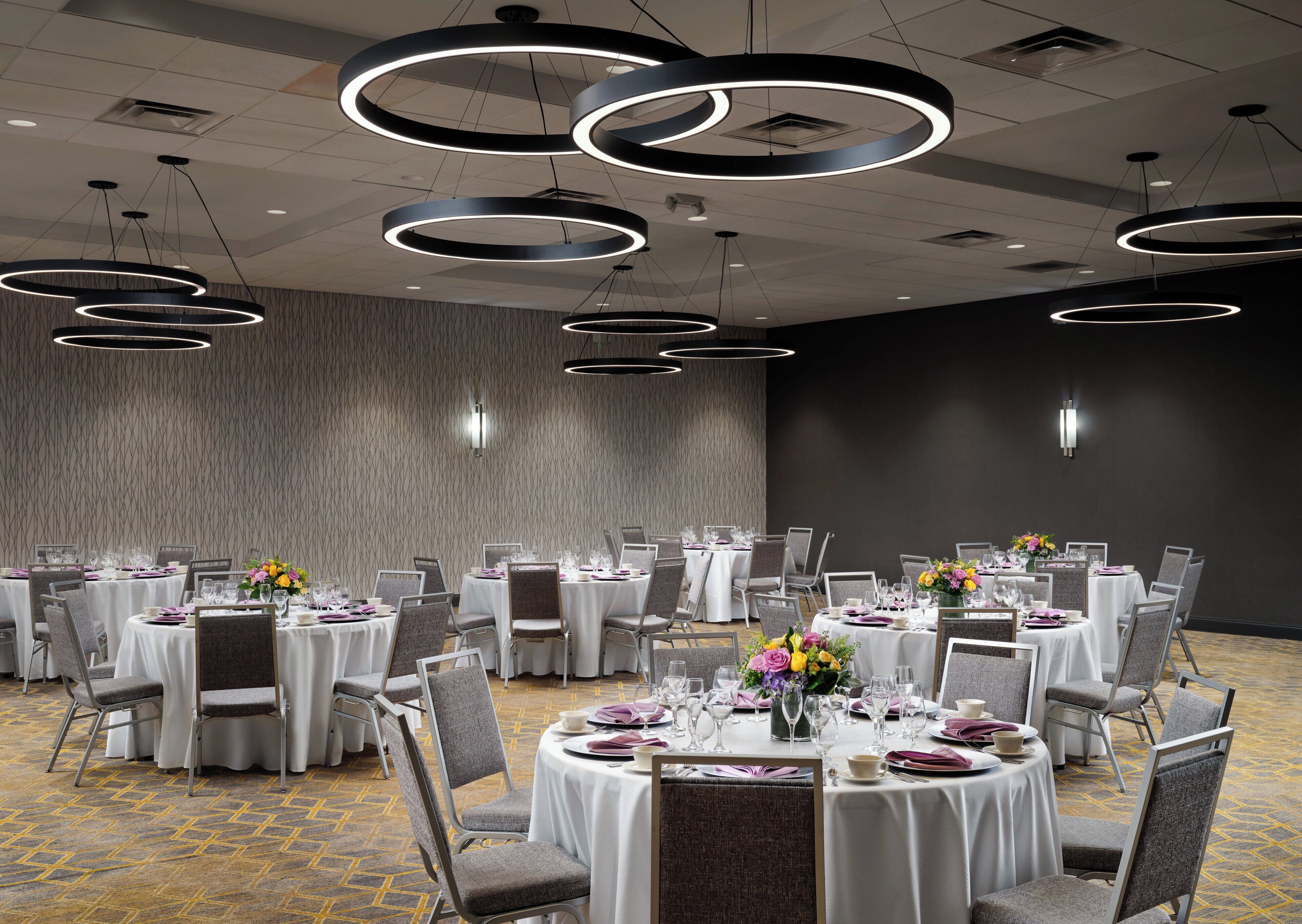 A banquet hall with round tables, chairs, and modern circular ceiling lights.