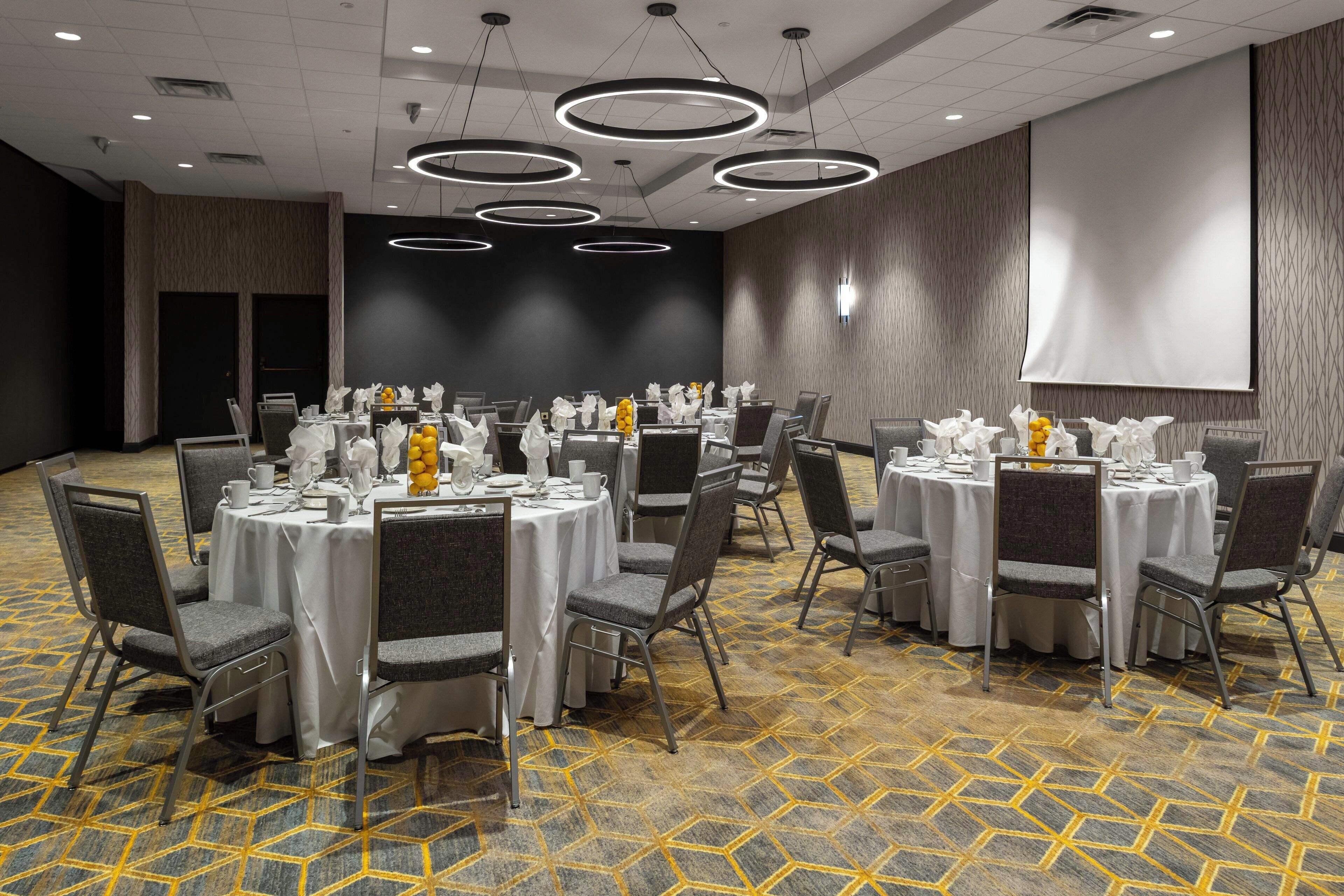 A conference room with round tables, grey chairs, and a carpeted floor.