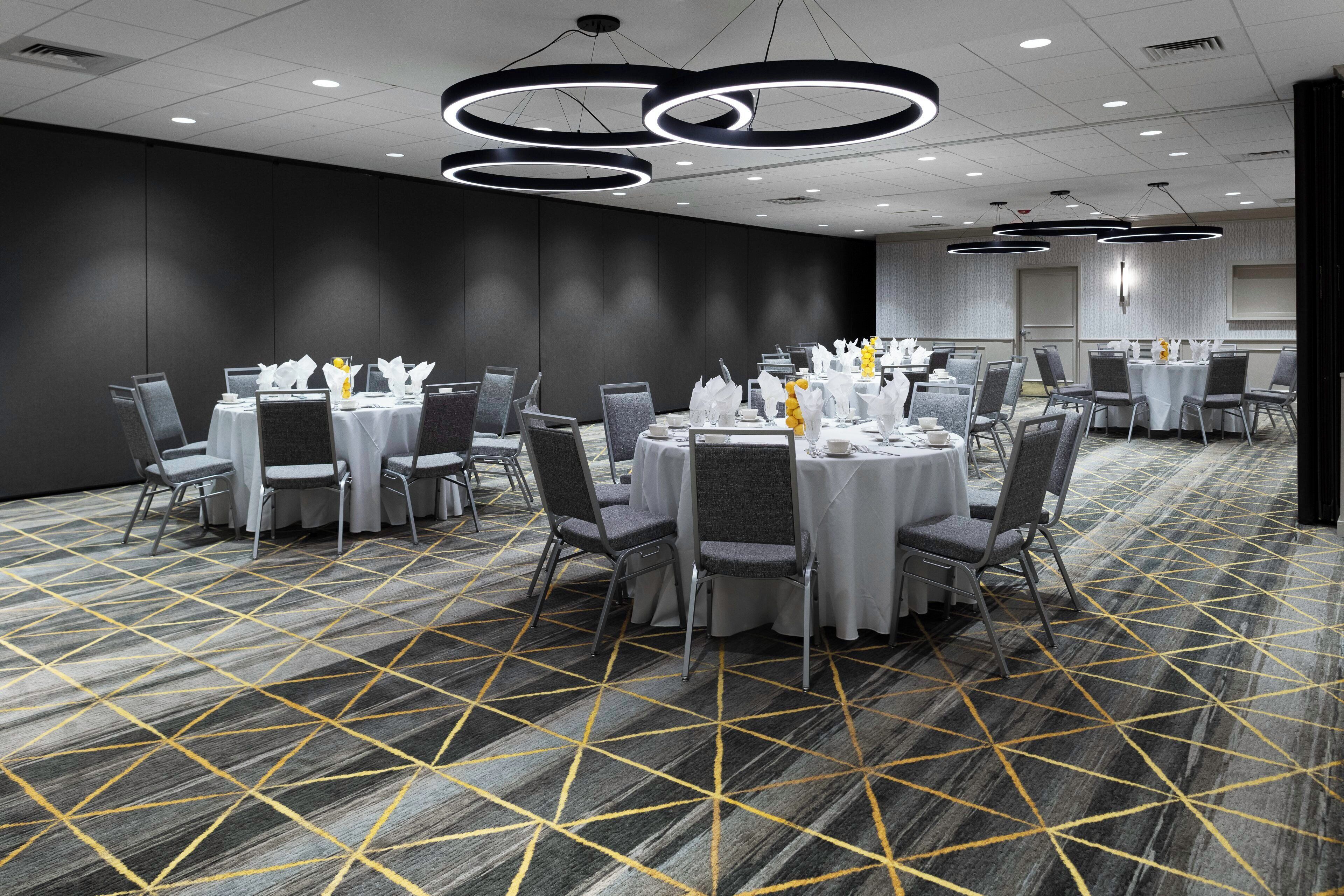 A conference room with round tables, grey chairs, and a patterned carpet.