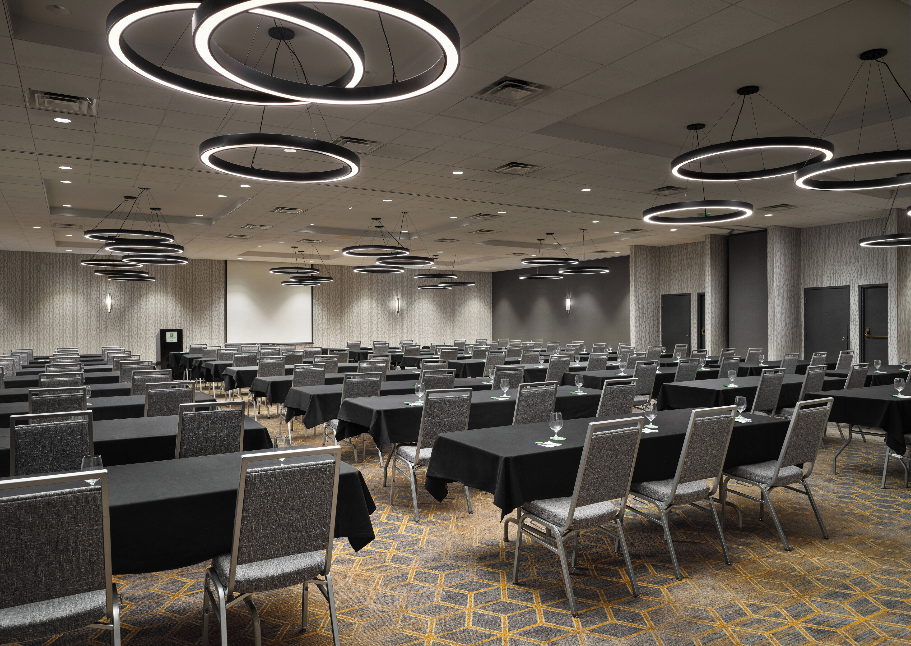 A conference room with multiple tables and chairs, circular ceiling lights, and a carpeted floor.