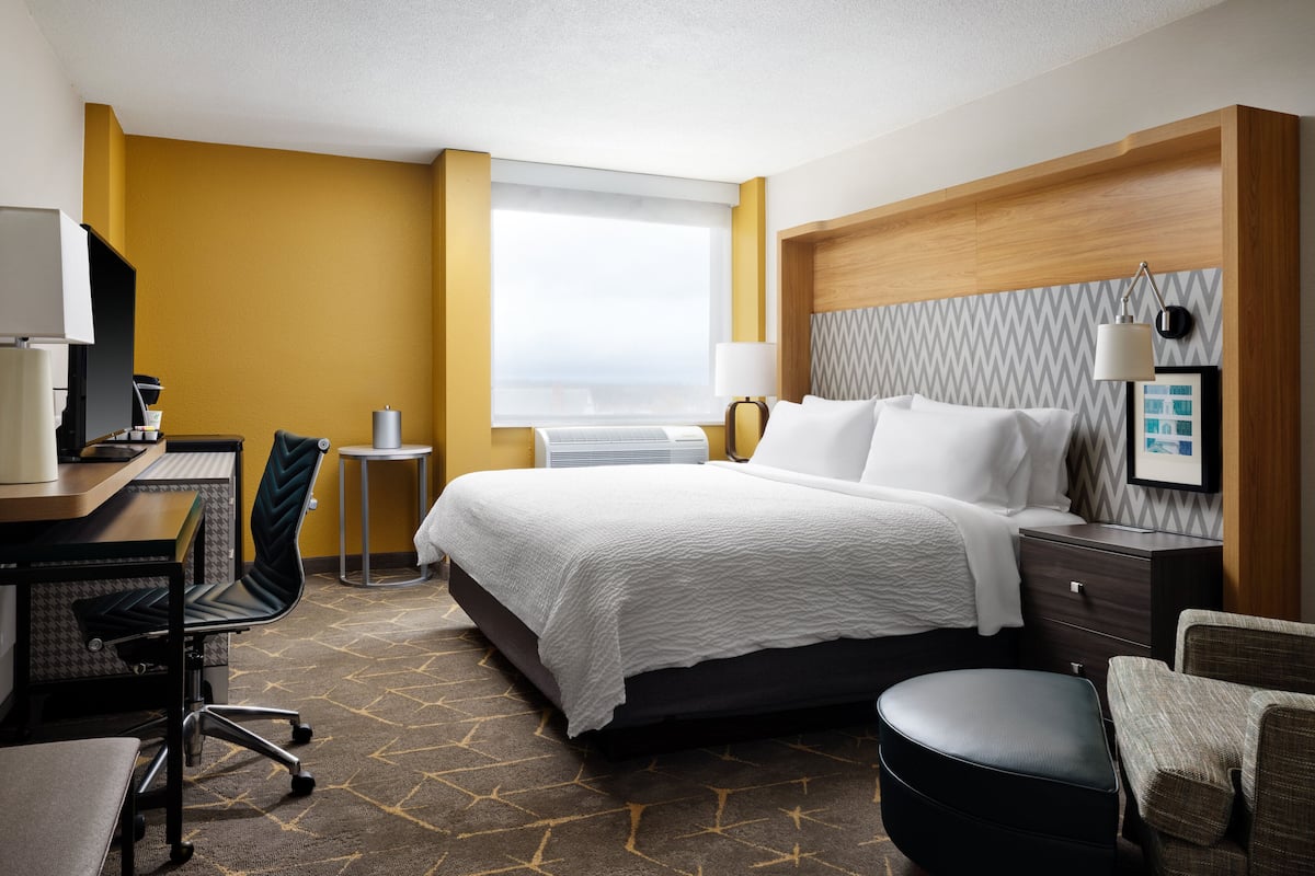 A hotel room with a bed, a desk, a chair, a small table, and a window.