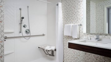 Un baño moderno con ducha, tocador con espejo y perchero.