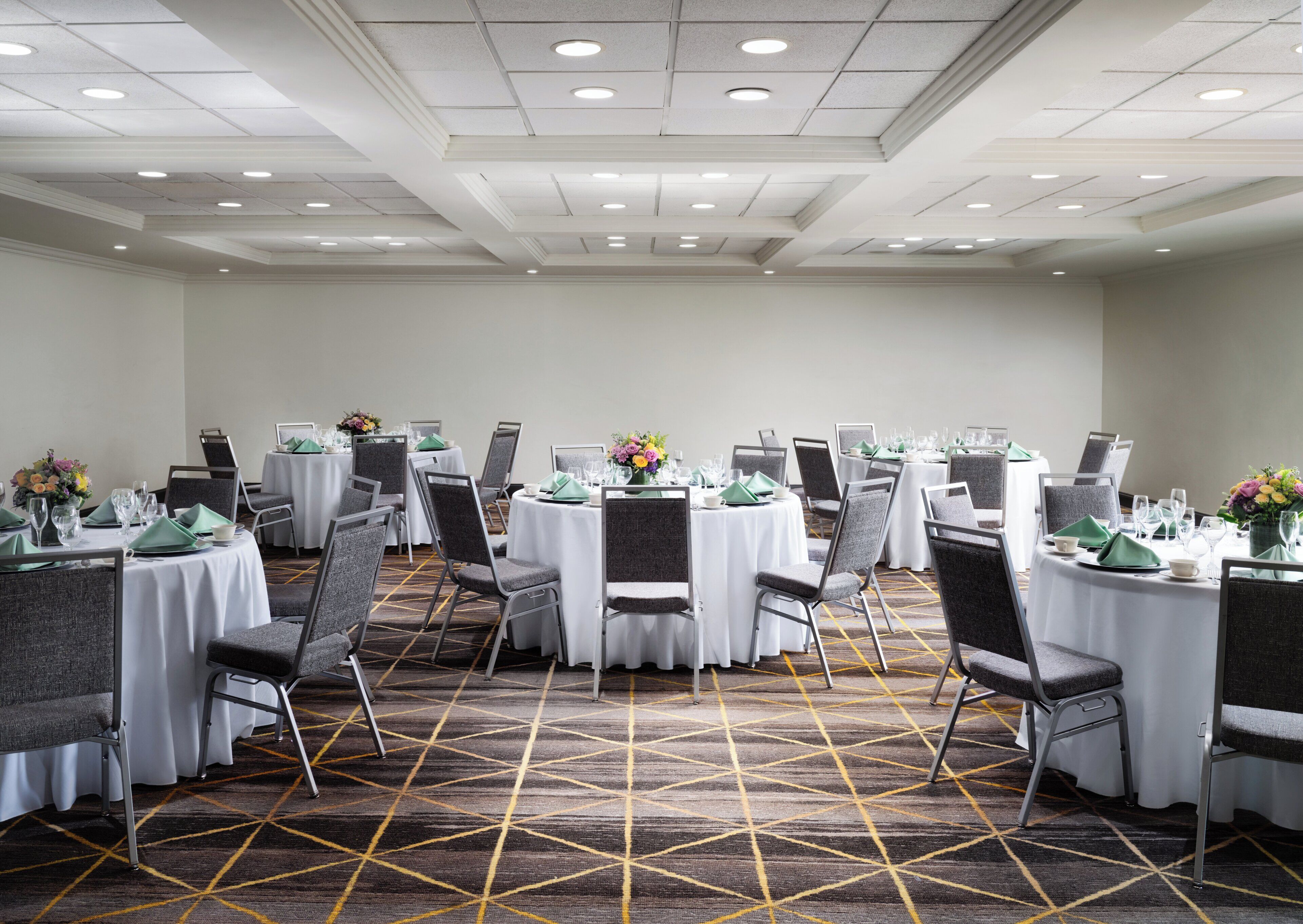 A conference room with round tables, gray chairs, and a patterned carpet.
