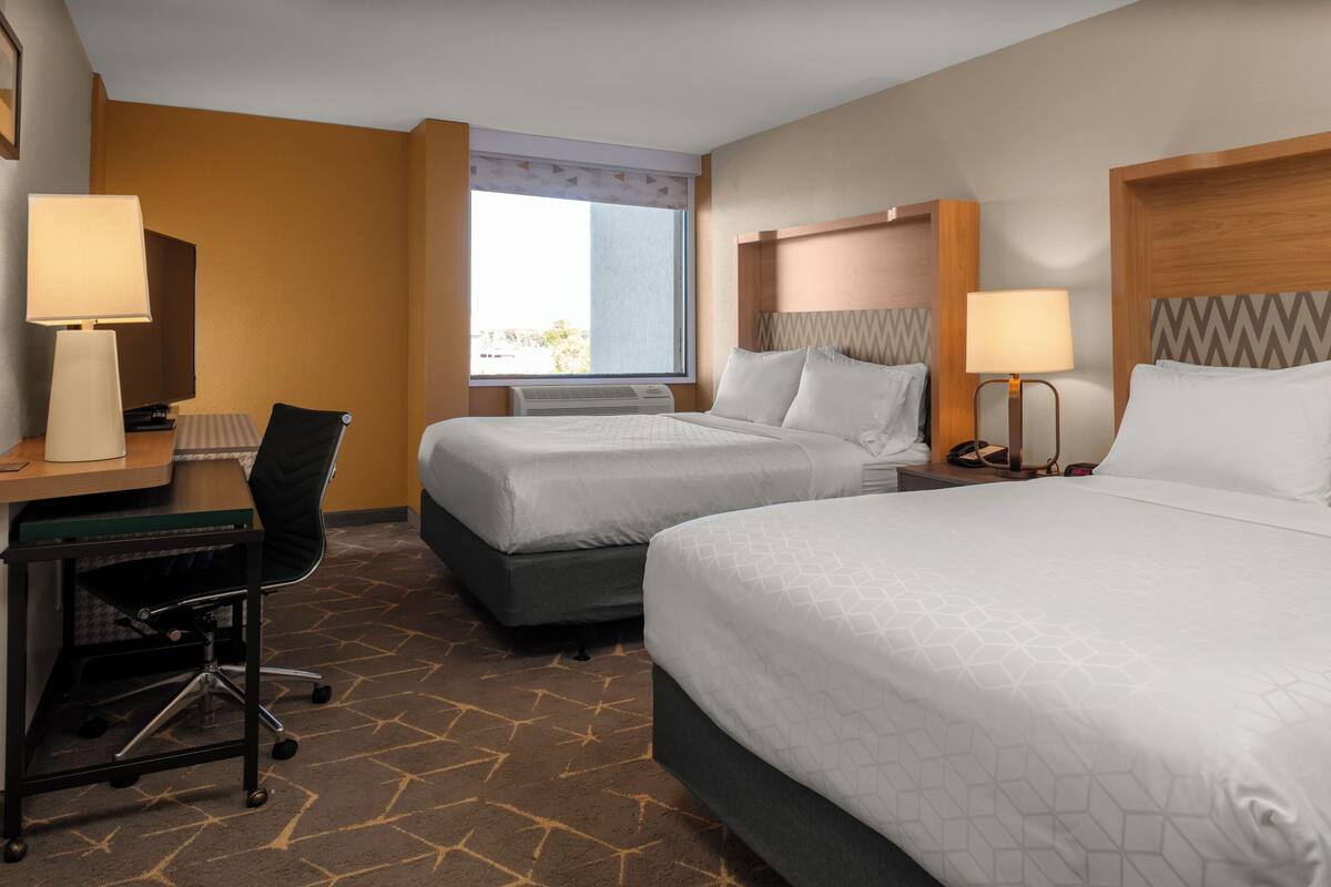 A hotel room with two beds, a desk with a chair, and a window with a view.