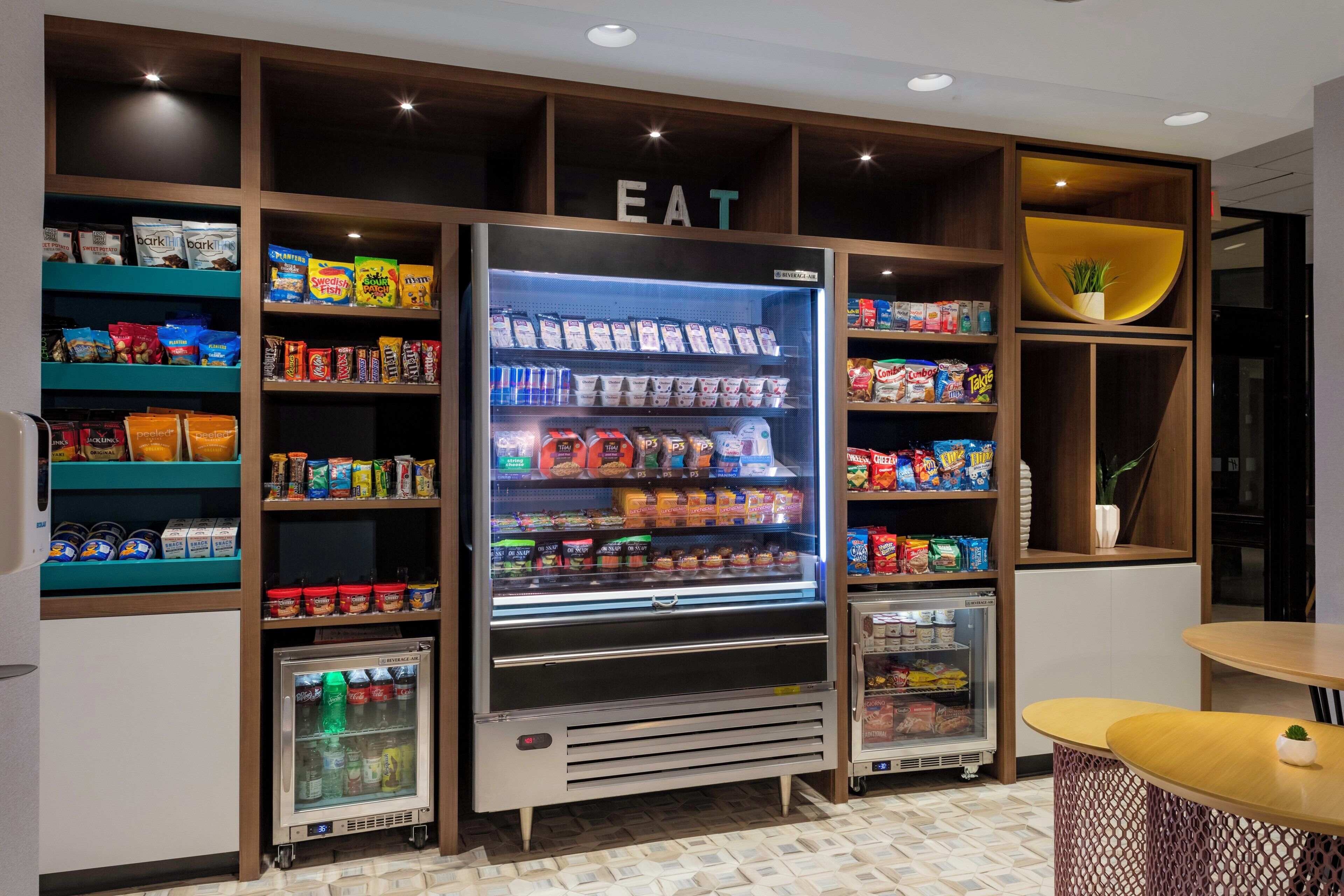 A snack vending area with multiple shelves stocked with various snacks and a beverage fridge.