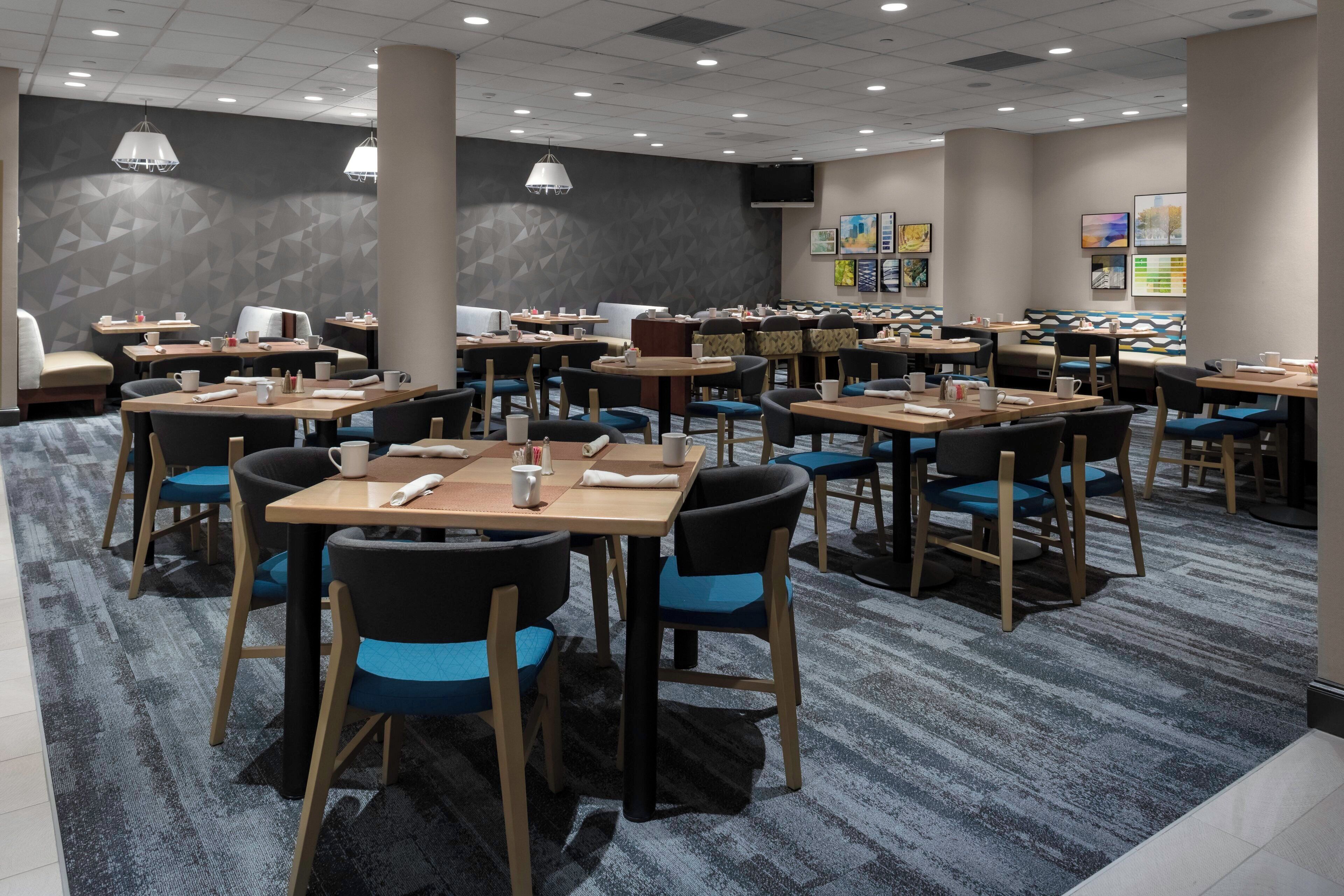 Un comedor de hotel con varias mesas y sillas, una alfombra estampada y decoración en las paredes.