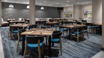Un comedor de hotel con varias mesas y sillas, una alfombra estampada y decoración en las paredes.