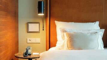 Una habitación de hotel con una cama, una mesita de noche con un teléfono, una lámpara de pared y un menú enmarcado en la pared.