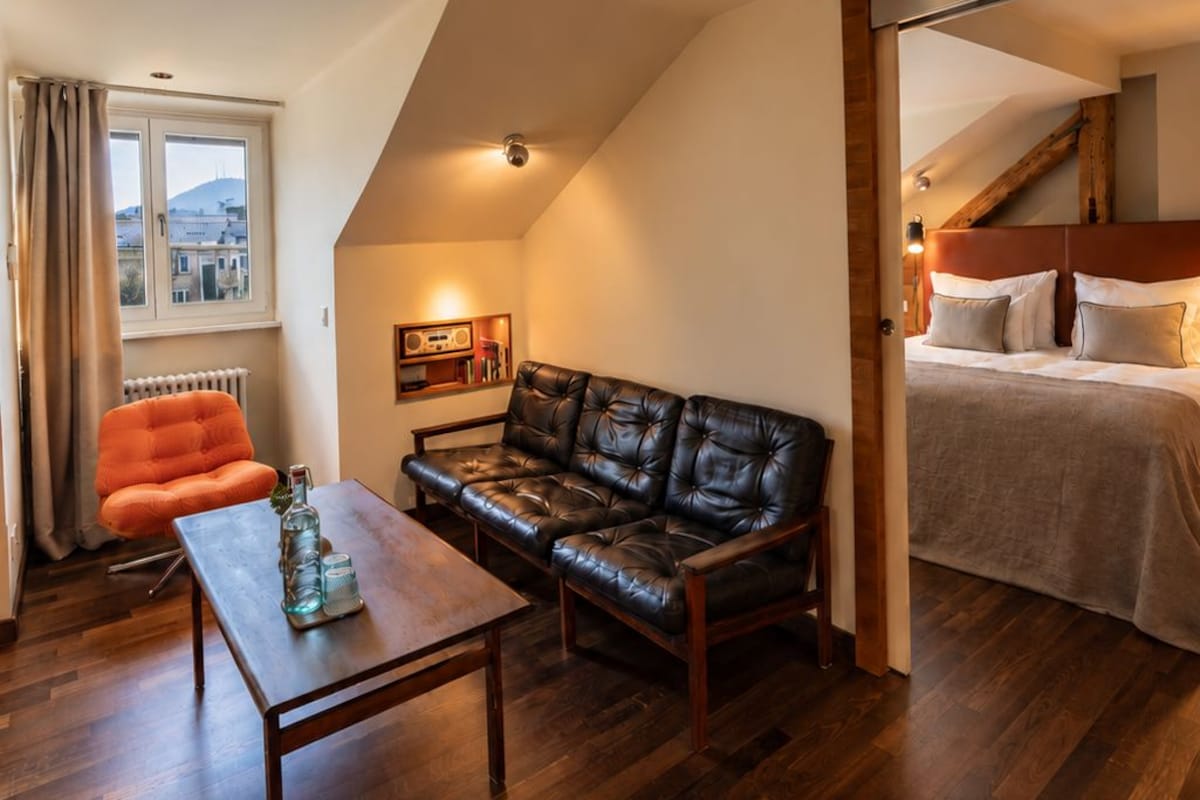 Una habitación acogedora con suelo de madera, un sofá de cuero, una mesita pequeña y una cama con cabecero.